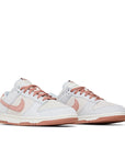 A pair of the Nike dunk low fossil rose skating shoes in rose and grey